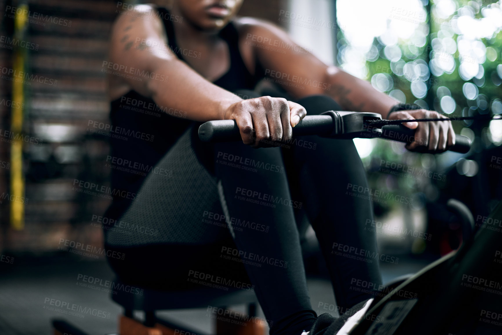 Buy stock photo Cropped shot of an unrecognizable young female athlete working out on a rowing machine in the gym