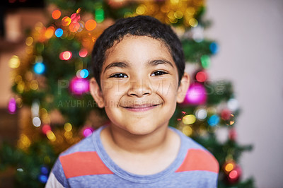 Buy stock photo Portrait of a cheerful little boy smiling at the camera with a Christmas tree in the background at home during the day