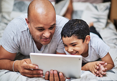 Buy stock photo Cropped shot of a cheerful young man and his son watching videos on a digital tablet while hanging out on a bed at home during the day