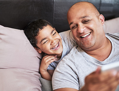 Buy stock photo Cropped shot of a cheerful young man and his son watching videos on a digital tablet together  while hanging out on a bed at home during the day