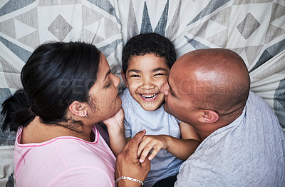 Buy stock photo Cropped shot of a cheerful young couple kissing their son on the cheek while hanging out on the bed at home during the day