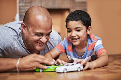Buy stock photo Cropped shot of a cheerful little boy and his father playing with toy cars while being seated on the floor at home during the day