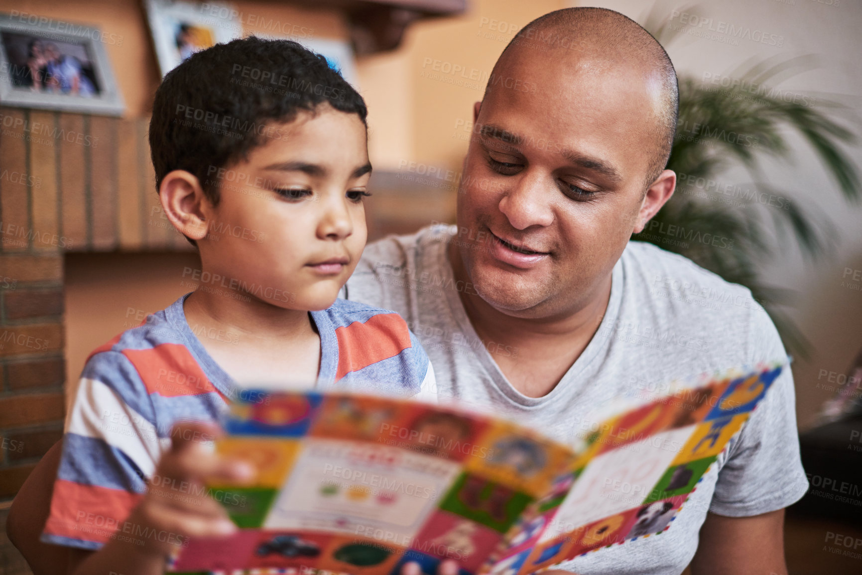 Buy stock photo Cropped shot of a cheerful little boy and his father reading a storybook together at home during the day