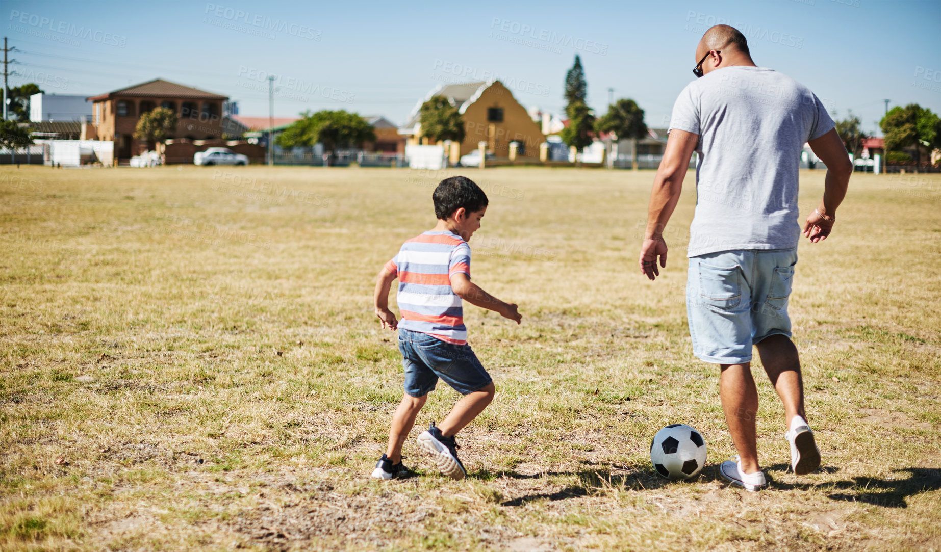 Buy stock photo Shot of a cheerful little boy and his father playing soccer together outside on a field during the day