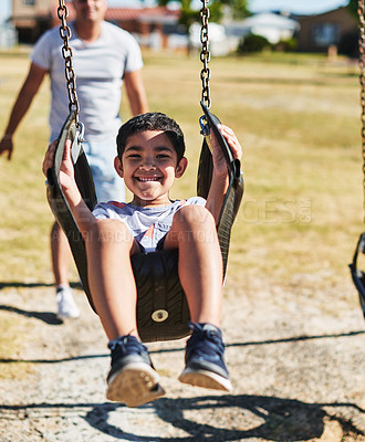 Buy stock photo Portrait of a cheerful little boy swinging on a swing outside in a park during the day
