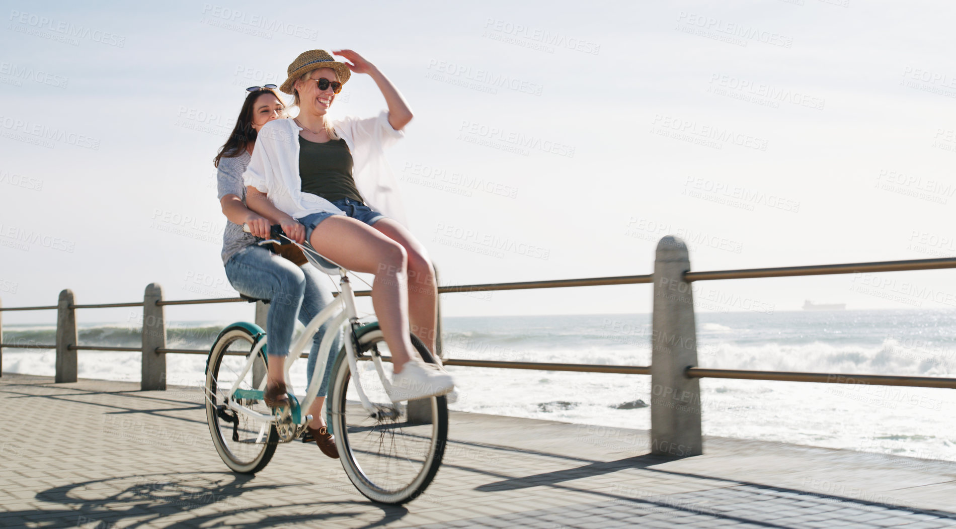 Buy stock photo Full length shot of a happy young couple riding a bicycle together on a promenade near the beach