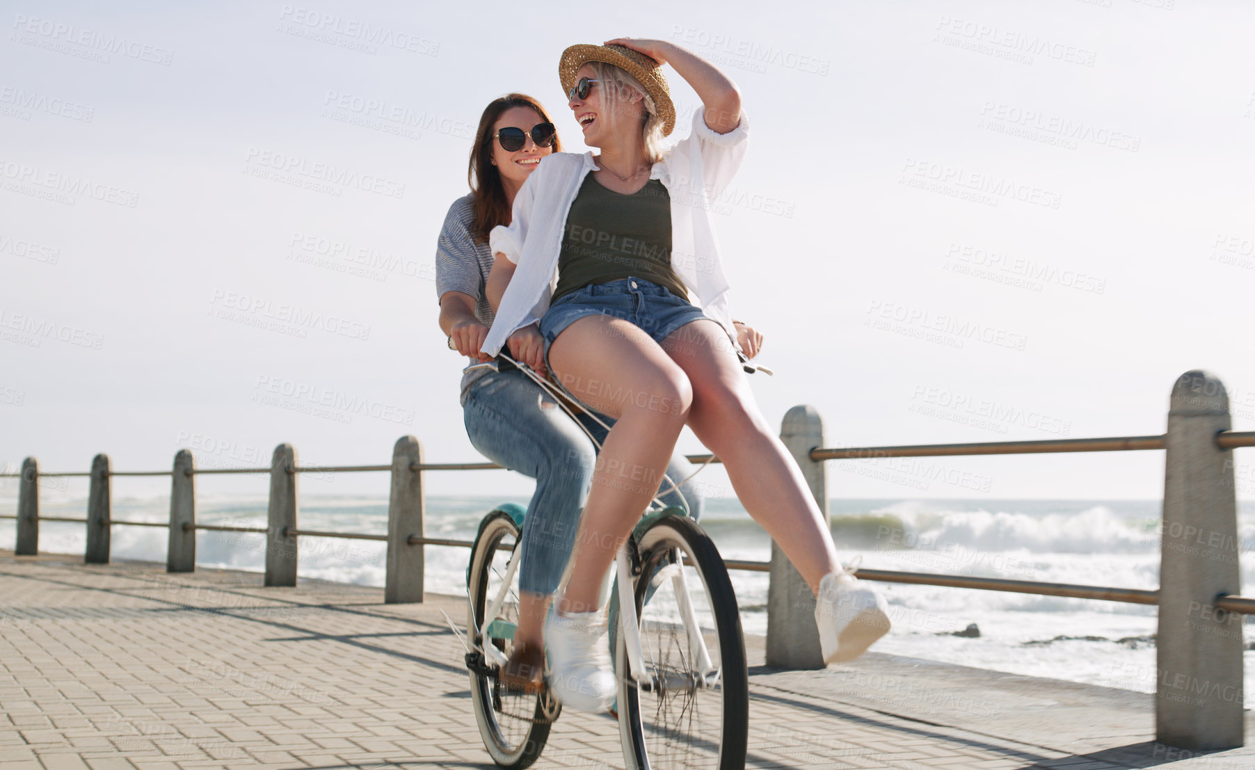 Buy stock photo Full length shot of a happy young couple riding a bicycle together on a promenade near the beach