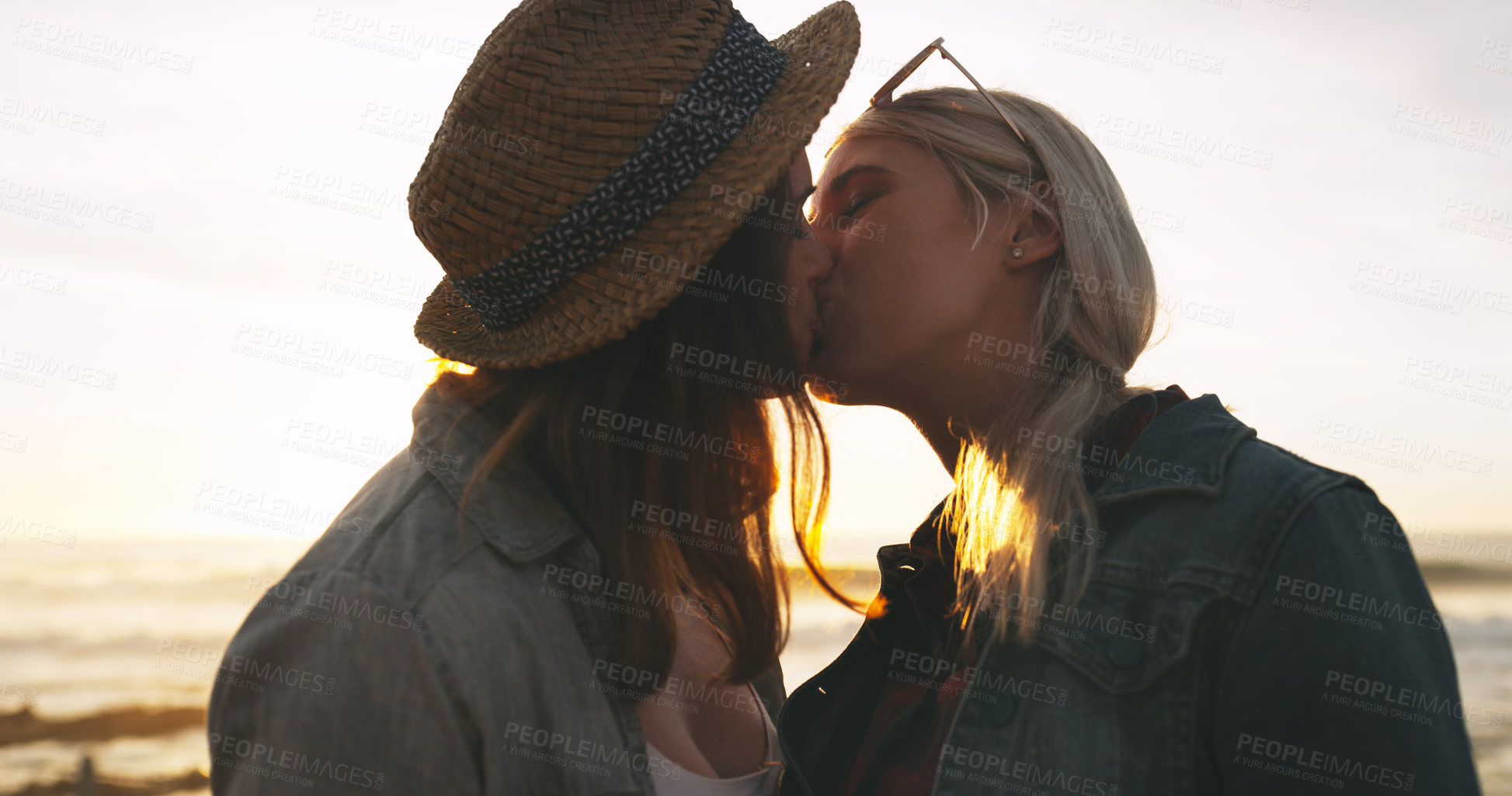 Buy stock photo Shot of an affectionate and happy young couple kissing while spending the day together outdoors near the beach