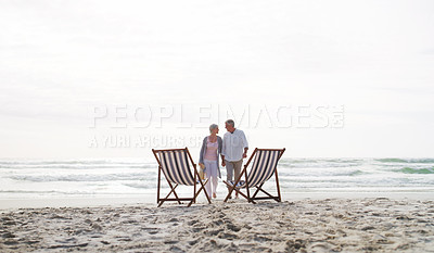 Buy stock photo Full length shot of an affectionate senior couple walking towards their loungers at the beach during the day