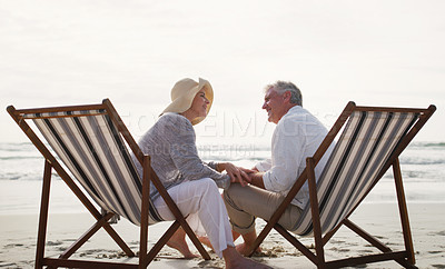 Buy stock photo Full length shot of an affectionate senior couple having an intimate chat while sitting on loungers at the beach