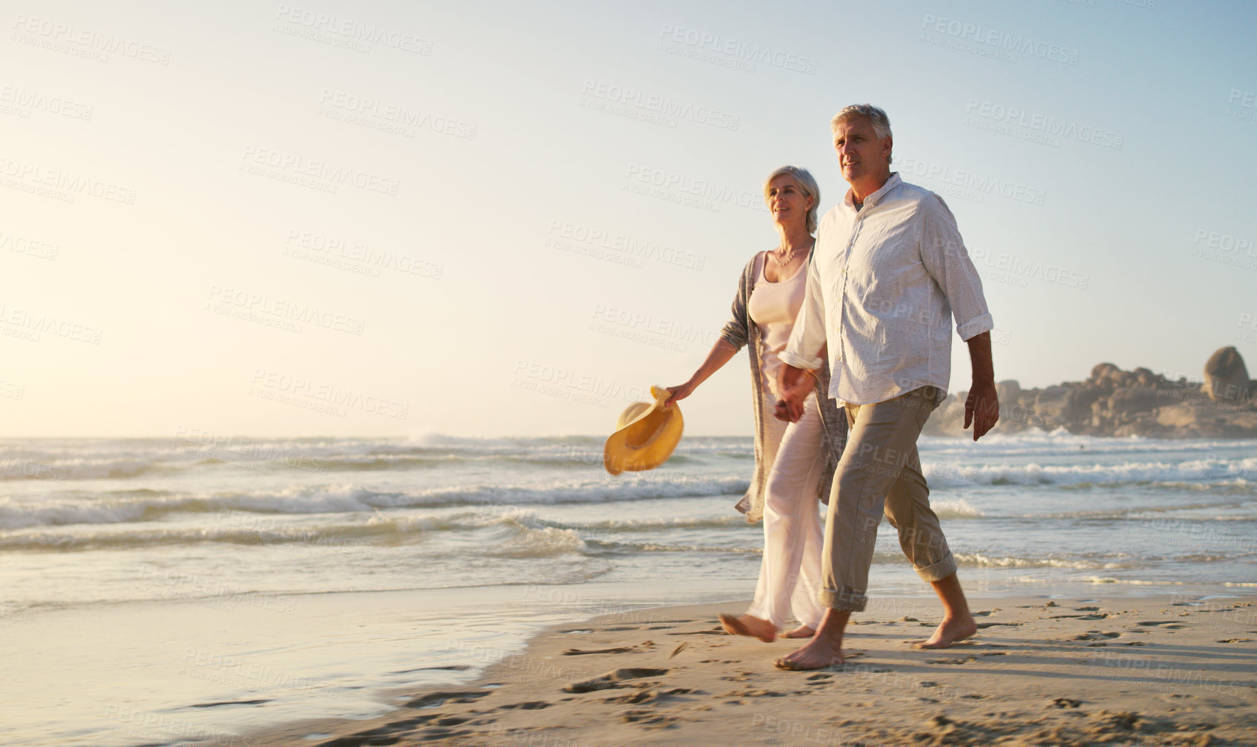 Buy stock photo Full length shot of an affectionate senior couple walking along the beach at sunset