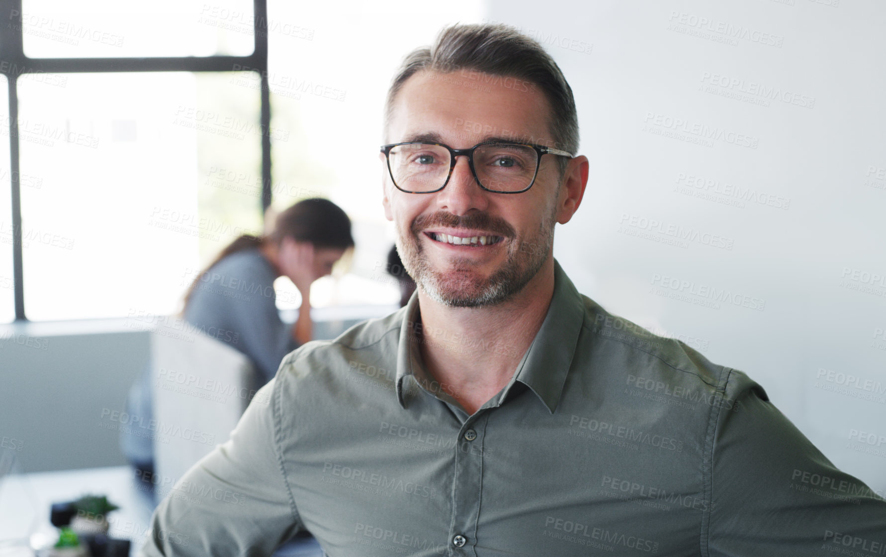 Buy stock photo Portrait of a confident mature businessman working in a modern office with his colleagues in the background