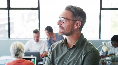 Buy stock photo Shot of a confident mature businessman working in a modern office with his colleagues in the background