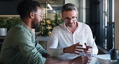 Buy stock photo Shot of two businessmen using a laptop and having a discussion in a modern office