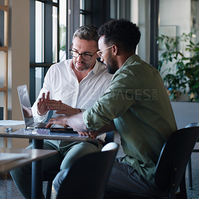 Buy stock photo Shot of two businessmen using a laptop and having a discussion in a modern office