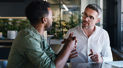 Buy stock photo Shot of two businessmen using a laptop and having a discussion in a modern office