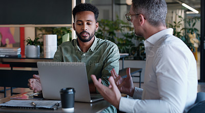 Buy stock photo Shot of two businessmen using a laptop and having a discussion in a modern office