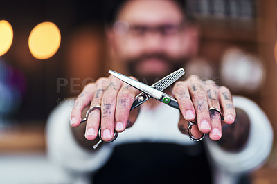 Buy stock photo Defocused shot of a young barber holding up a pair of scissors inside his barbershop
