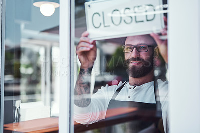 Buy stock photo Cropped shot of a handsome young barber hanging up a closed sign on the window of his barbershop