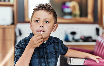 Buy stock photo Portrait of an adorable little boy eating a lollipop after getting a fresh haircut at a salon