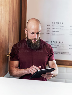 Buy stock photo Cropped shot of a handsome young barber using a digital tablet while working inside his barbershop