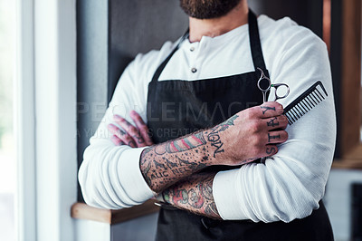 Buy stock photo Cropped shot of a unrecognizable tattooed barber posing with a pair of scissors and a hair comb inside a barbershop