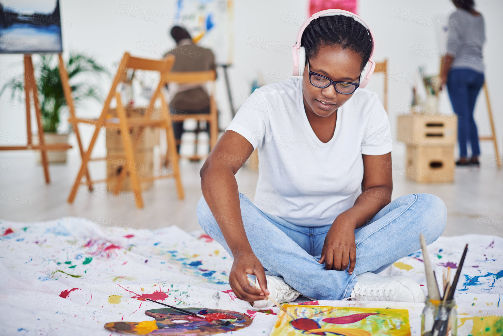 Buy stock photo Shot of a young woman wearing headphones while painting in a art studio