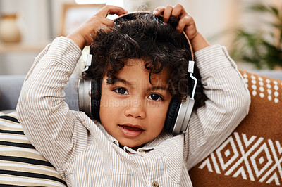 Buy stock photo Portrait of an adorable little boy listening to music on headphones while sitting on a sofa at home