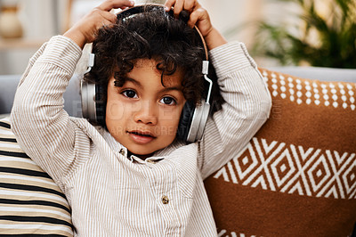 Buy stock photo Portrait of an adorable little boy listening to music on headphones while sitting on a sofa at home