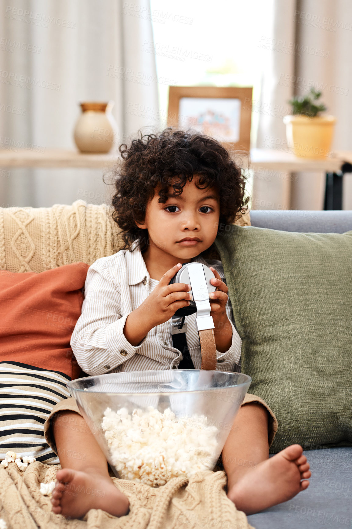 Buy stock photo Full length shot of an adorable little boy eating popcorn and listening to music on headphones at home