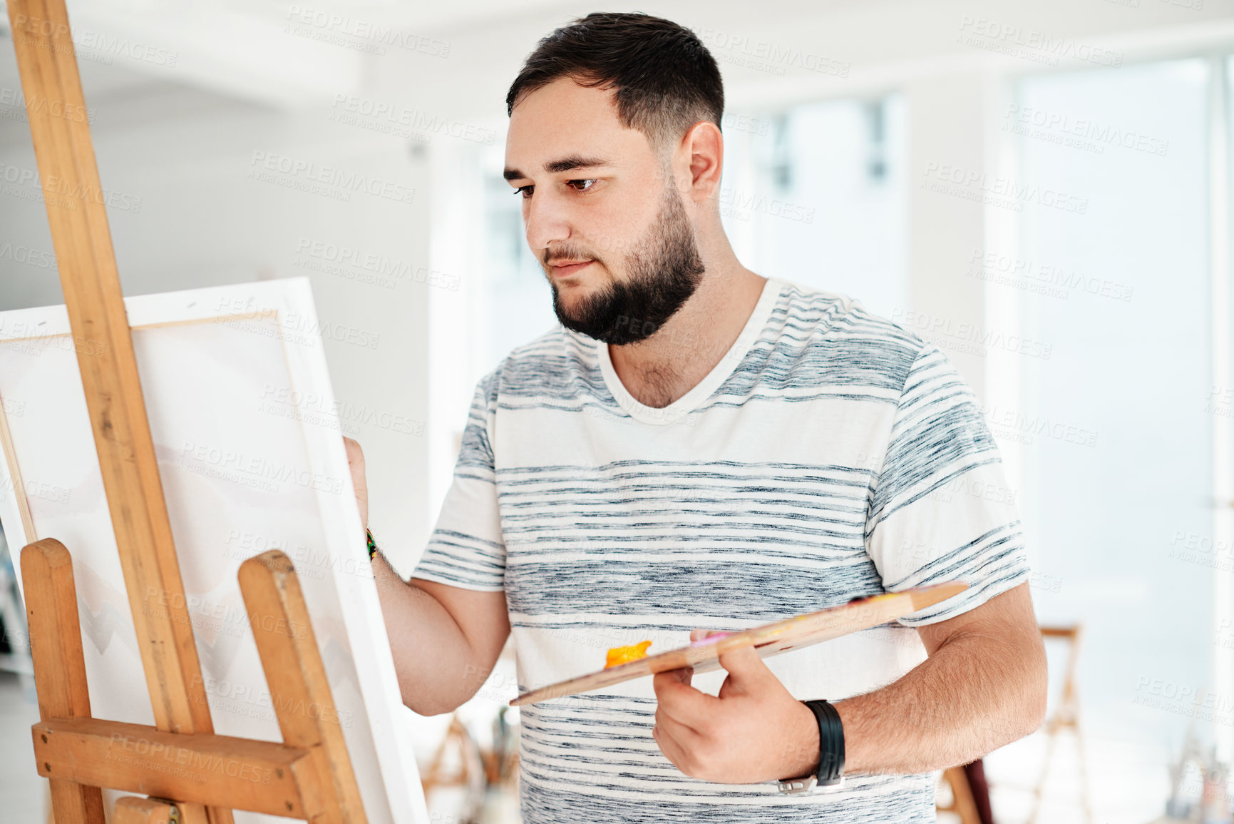 Buy stock photo Cropped shot of a handsome young artist standing alone and painting during an art class in the studio