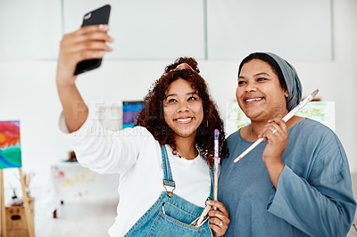 Buy stock photo Cropped shot of two attractive young women standing and using a cellphone to take a selfie during an art class