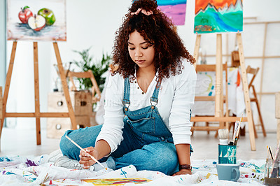 Buy stock photo Full length shot of an attractive young artist sitting alone and painting during an art class in the studio