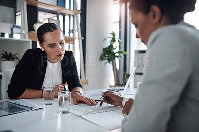 Buy stock photo Cropped shot of two attractive young businesswomen filling out paperwork together inside an office