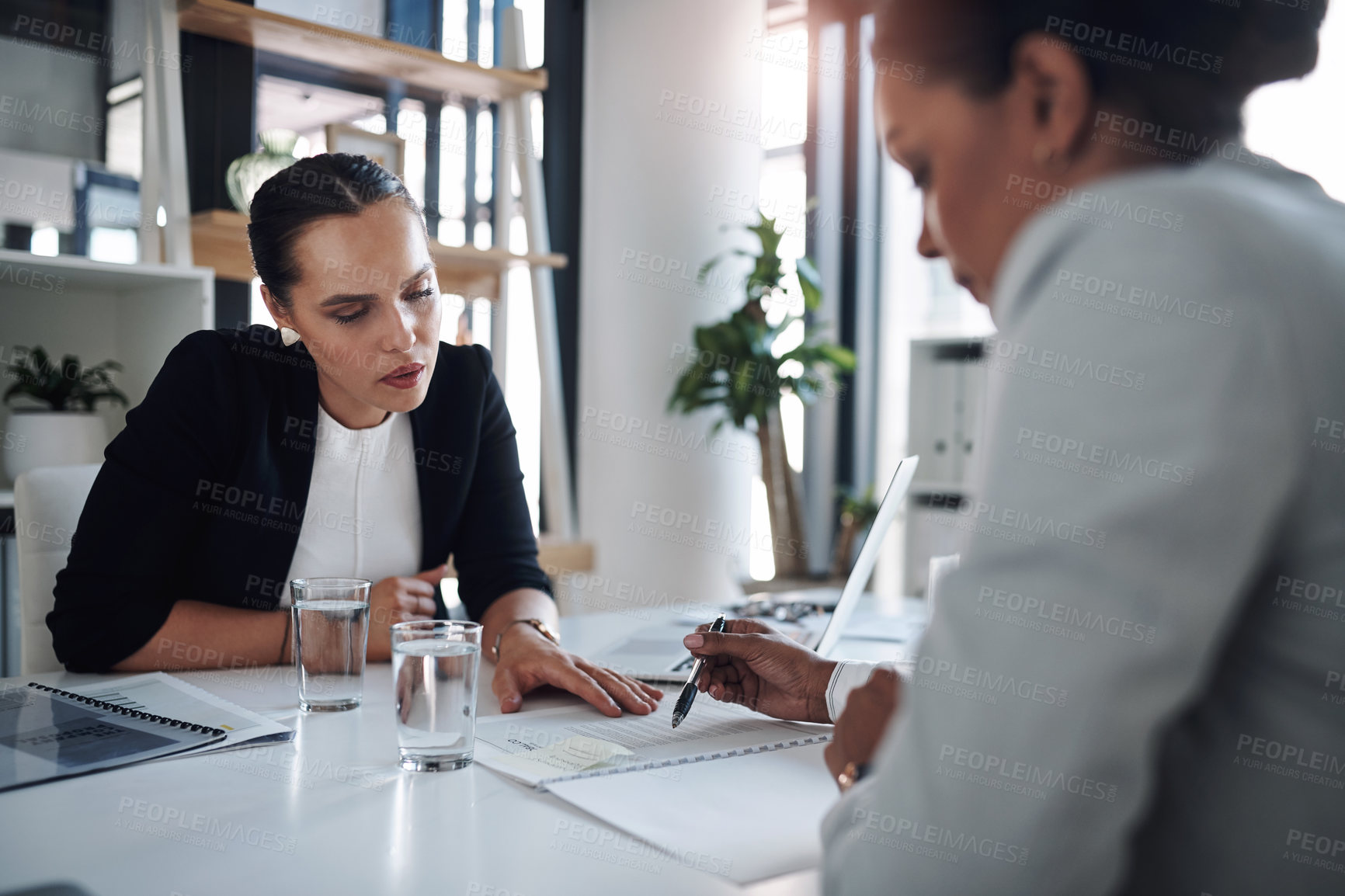 Buy stock photo Cropped shot of two attractive young businesswomen filling out paperwork together inside an office