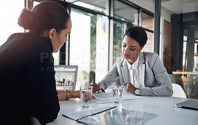 Buy stock photo Cropped shot of two attractive young businesswomen filling out paperwork together inside an office