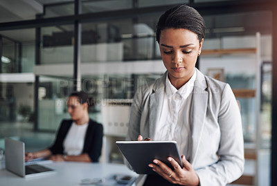 Buy stock photo Cropped shot of an attractive young businesswoman using a digital tablet inside an office with her colleague in the background