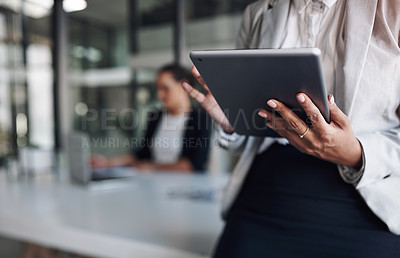 Buy stock photo Cropped shot of an unrecognizable businesswoman using a digital tablet inside an office with her colleague in the background