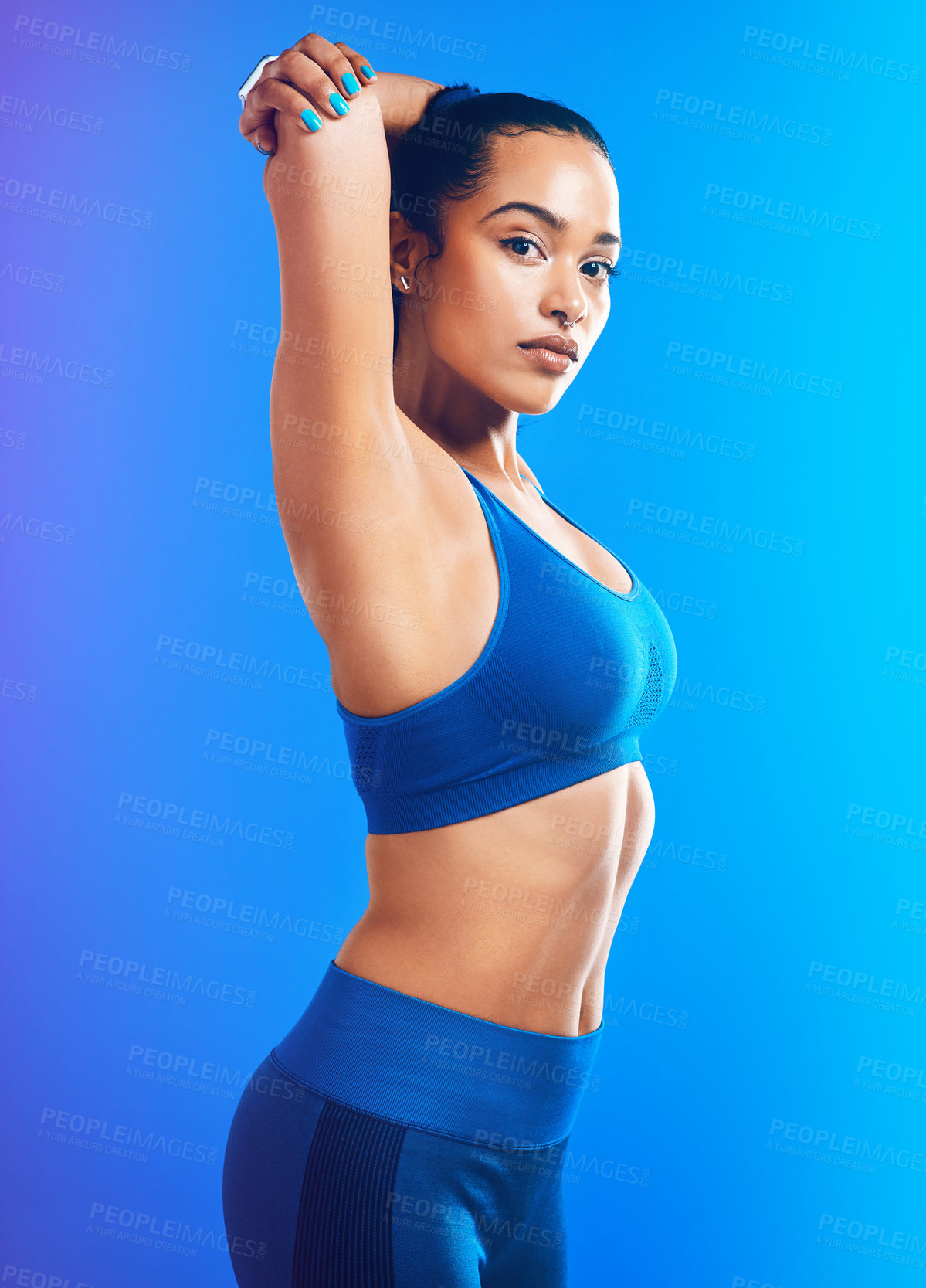 Buy stock photo Studio portrait of an attractive young sportswoman stretching her arms against a blue background