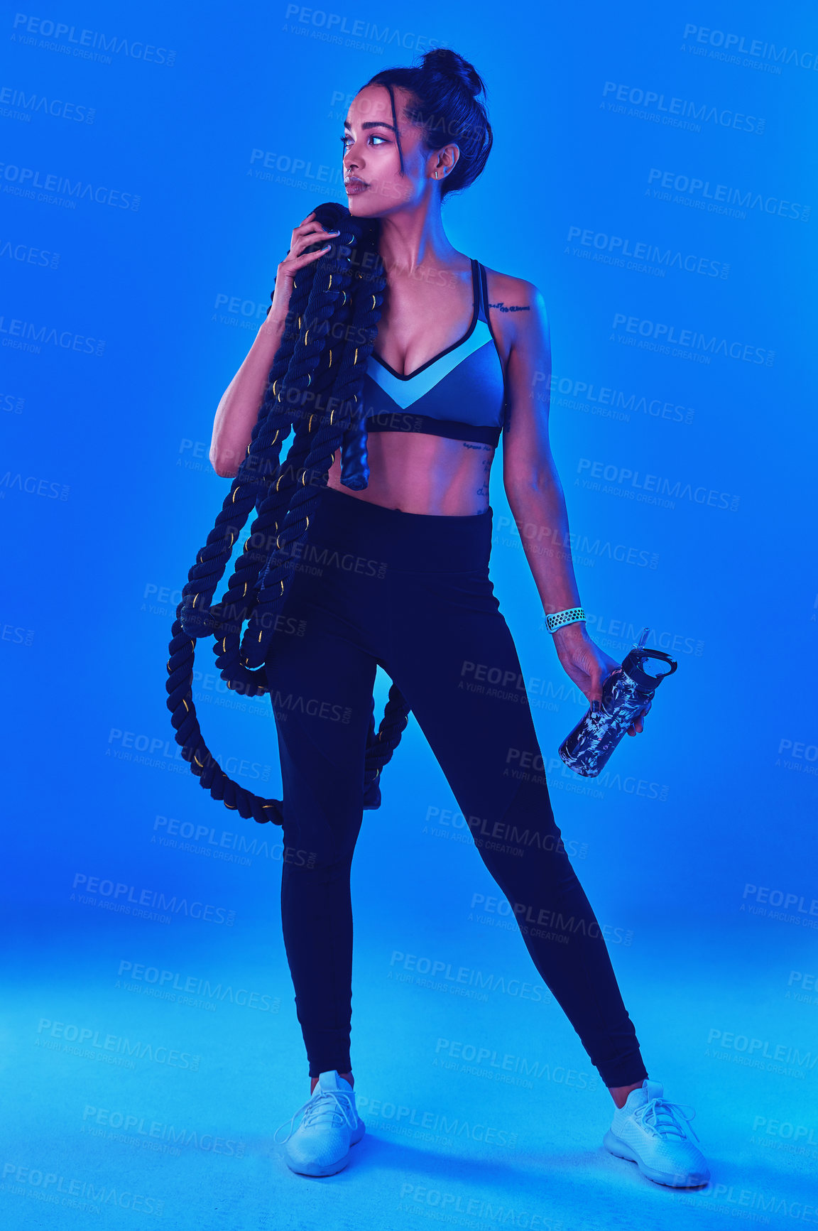 Buy stock photo Full length shot of an attractive young sportswoman posing carrying battle ropes against a blue background
