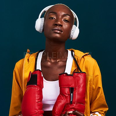 Buy stock photo Cropped portrait of an attractive young female boxer standing alone and posing with headphones on against a dark studio background
