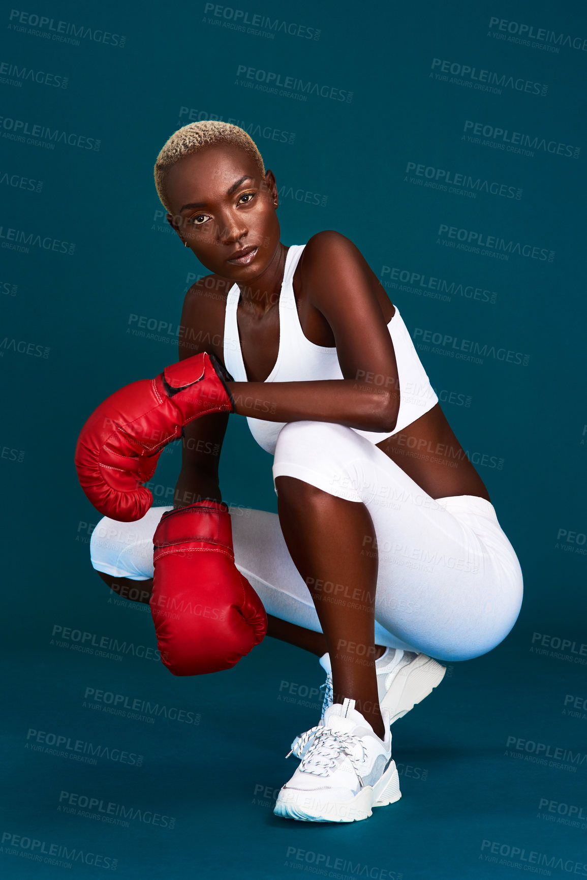 Buy stock photo Full length portrait of an attractive young female boxer crouching against a dark background with her boxing gloves on
