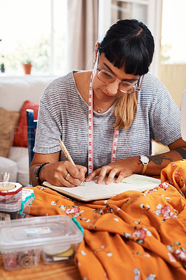 Buy stock photo Cropped shot of a young woman making notes while designing a garment at home