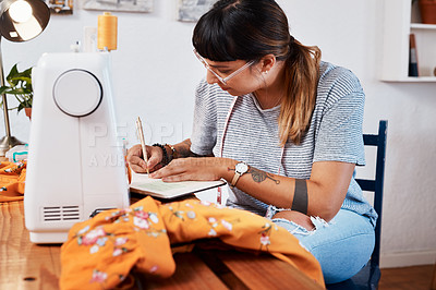 Buy stock photo Cropped shot of a young woman making notes while designing a garment at home