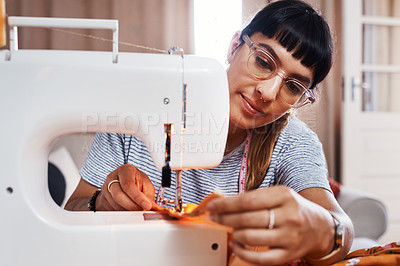 Buy stock photo Cropped shot of a young woman stitching fabric using a sewing machine at home