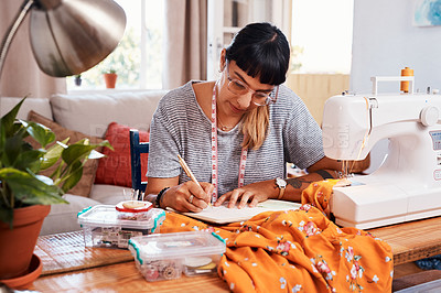 Buy stock photo Shot of a beautiful young woman making notes while working on a garment at home
