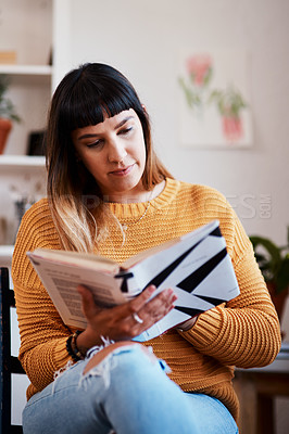 Buy stock photo Cropped shot of a beautiful young woman reading a book while relaxing at home