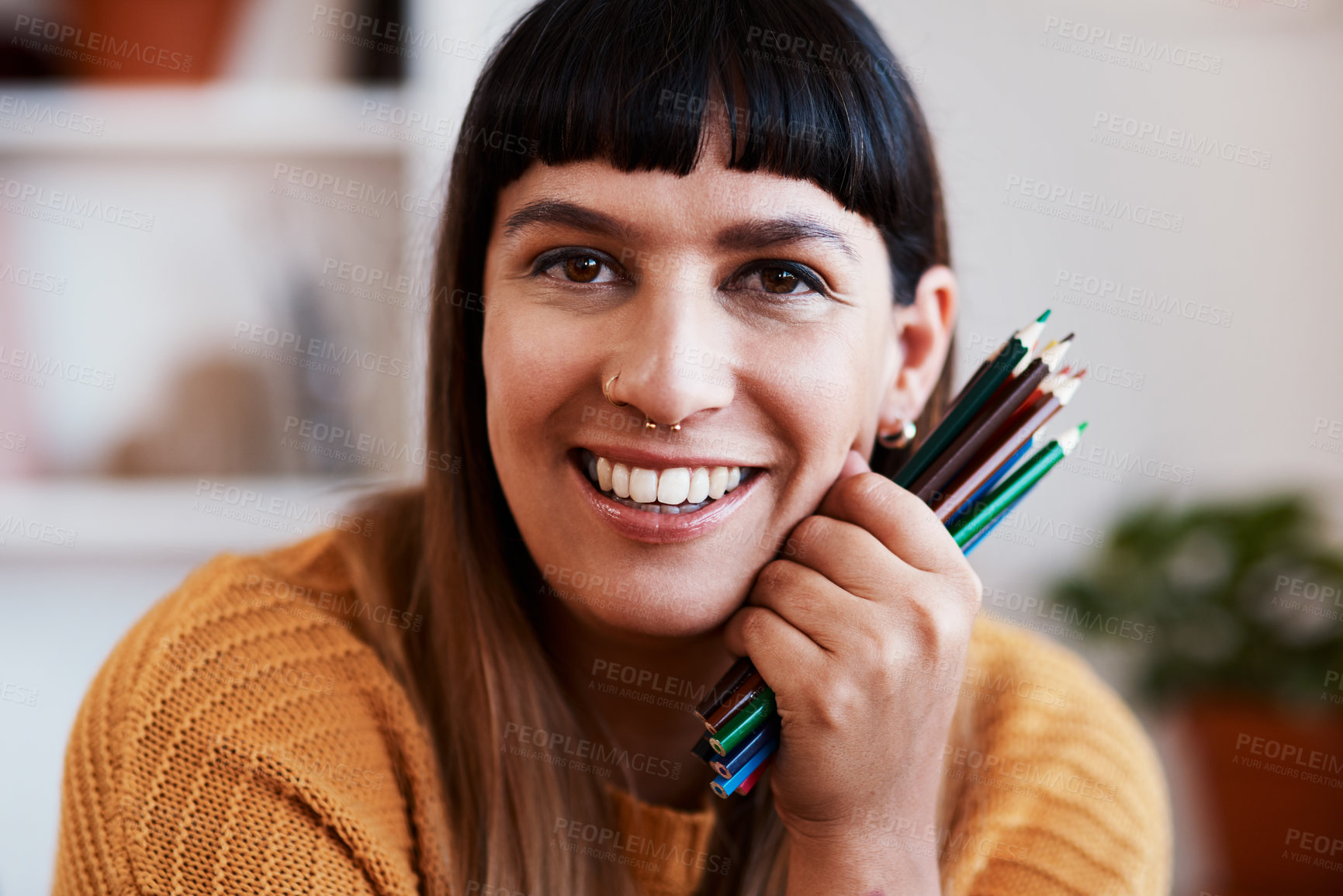 Buy stock photo Shot of an attractive young woman holding coloring pencils while relaxing at home