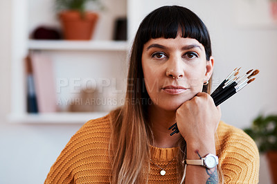 Buy stock photo Shot of an attractive young woman holding paintbrushes while relaxing at home
