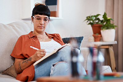 Buy stock photo Shot of an attractive young woman writing while relaxing at home